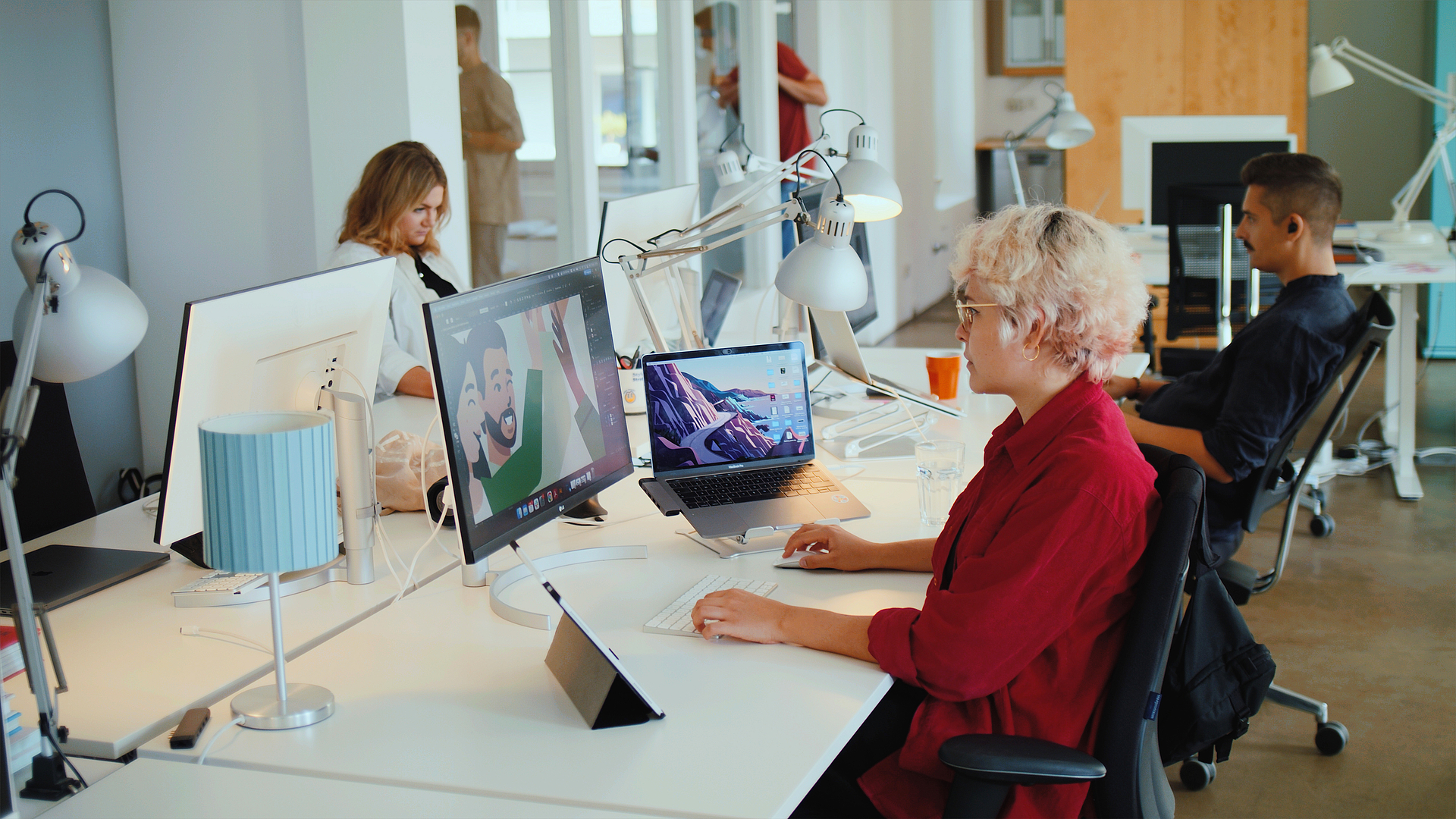 Drei Mitarbeitende der Designagentur Radikant sitzen an Schreibtischen und arbeiten an Computern in einem Büro